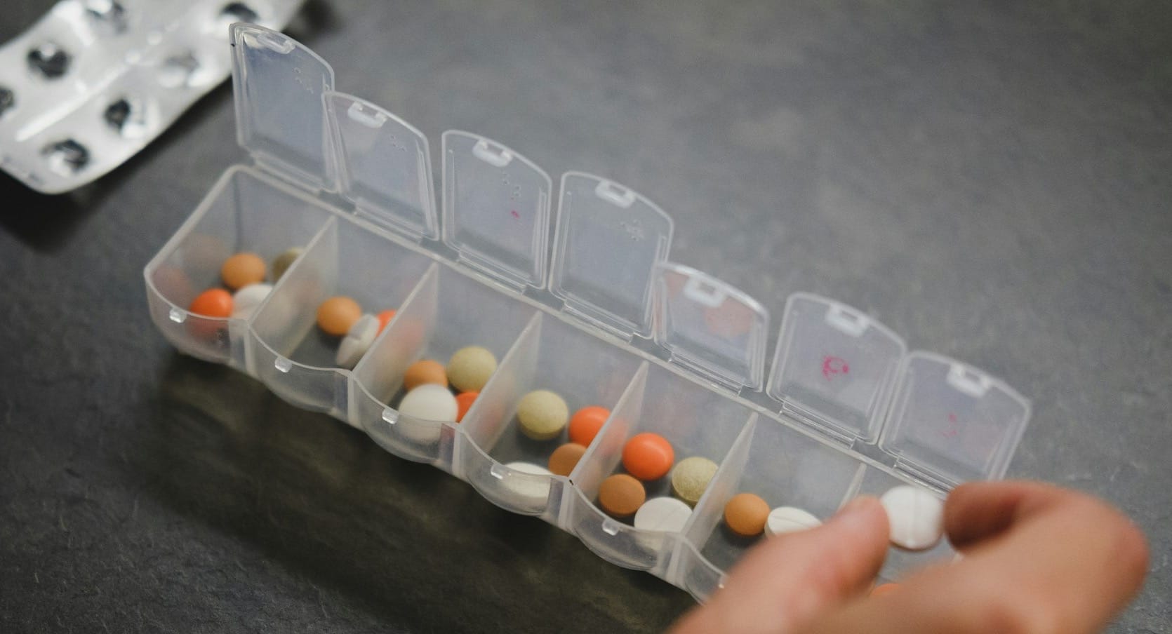 person about to pick medicine from medicine organizer